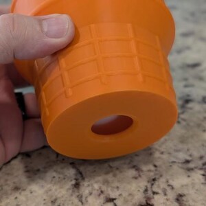 May include: Orange plastic drain stopper with a black rubber ring. The stopper has a grid pattern and a hole in the center.