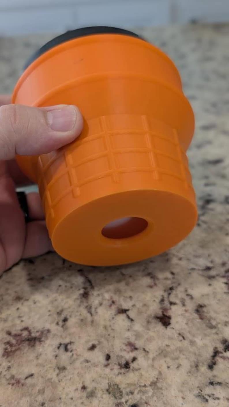 May include: Orange plastic drain stopper with a black rubber ring. The stopper has a grid pattern and a hole in the center.