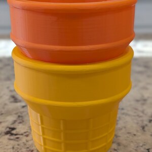 May include: Two plastic ice cream cones, one orange and one yellow, stacked on top of each other.