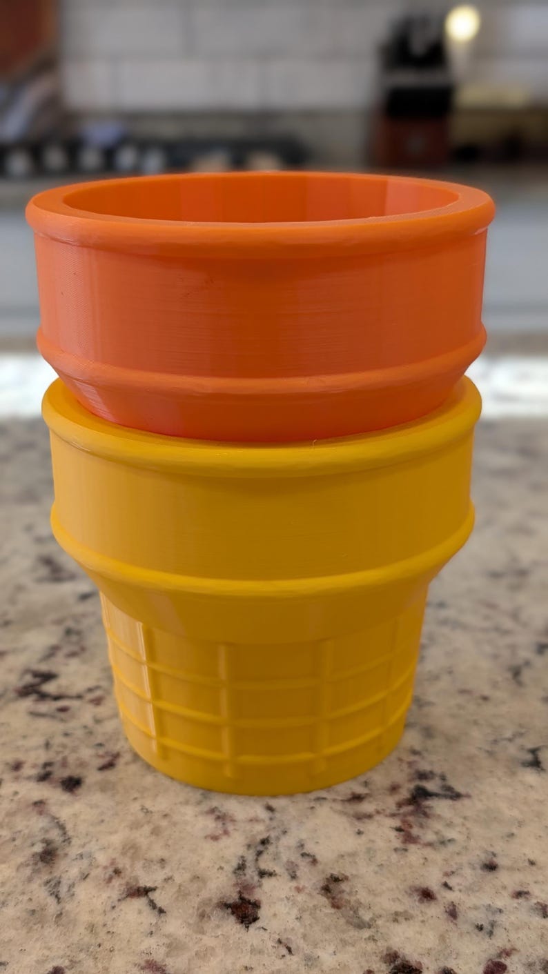 May include: Two plastic ice cream cones, one orange and one yellow, stacked on top of each other.
