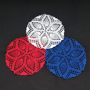 Può includere: Tre tovagliette all'uncinetto in rosso, bianco e blu. Le tovagliette sono circolari e hanno un design delicato e traforato.