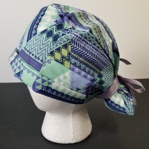 May include: A green and purple patterned surgical scrub hat with a ponytail hole and a purple ribbon tie.