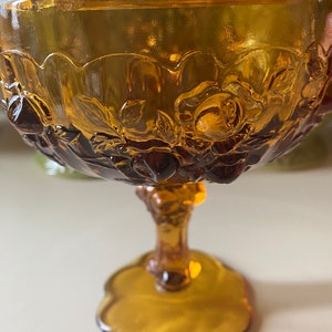 K&ouml;nnte beinhalten: Amberfarbene Glassch&uuml;ssel mit Fu&szlig; und Blumenmuster. Die Sch&uuml;ssel hat einen gewellten Rand und ein erhabenes Rosenmuster.