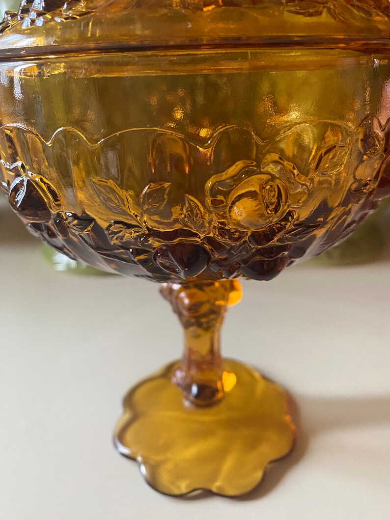 K&ouml;nnte beinhalten: Amberfarbene Glassch&uuml;ssel mit Fu&szlig; und Blumenmuster. Die Sch&uuml;ssel hat einen gewellten Rand und ein erhabenes Rosenmuster.