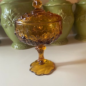 K&ouml;nnte beinhalten: Eine antike Bonboniere aus bernsteinfarbenem Glas mit Deckel und einem Sockel. Die Schale ist mit einem Blumenmuster verziert und hat einen gewellten Rand.