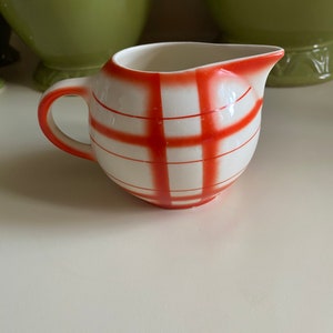 Może przedstawiać: Mały biały dzbanek do śmietanki z czerwono-białym wzorem w kratkę.