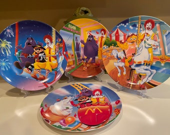 Może przedstawiać: Zestaw czterech kolorowych ceramicznych talerzy z postaciami z McDonald's. Talerze przedstawiają diabelski młyn, karuzelę, kolejkę górską i krzywe zwierciadło. Talerze są w doskonałym stanie i byłyby świetnym dodatkiem do kolekcji każdego kolekcjonera McDonald's.