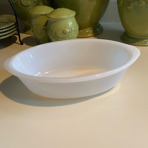 May include: White oval baking dish with a slightly raised rim. The dish is made of ceramic and has a smooth, glossy finish.