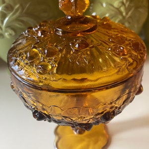 K&ouml;nnte beinhalten: Amberfarbene Glassch&uuml;ssel mit Blumenmuster und einem Knopfdeckel. Die Sch&uuml;ssel hat einen Sockel.