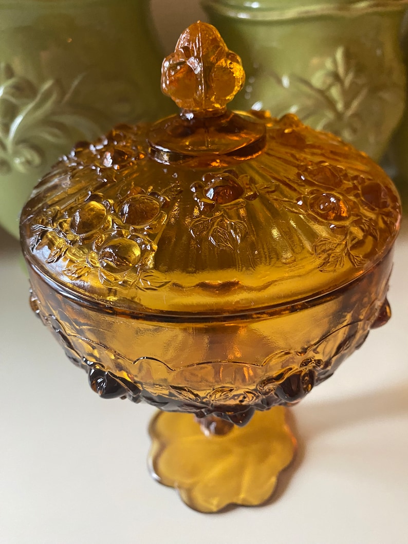 K&ouml;nnte beinhalten: Amberfarbene Glassch&uuml;ssel mit Blumenmuster und einem Knopfdeckel. Die Sch&uuml;ssel hat einen Sockel.