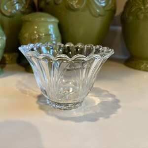 May include: A clear glass bowl with a scalloped edge and a fluted design. The bowl is sitting on a white surface.