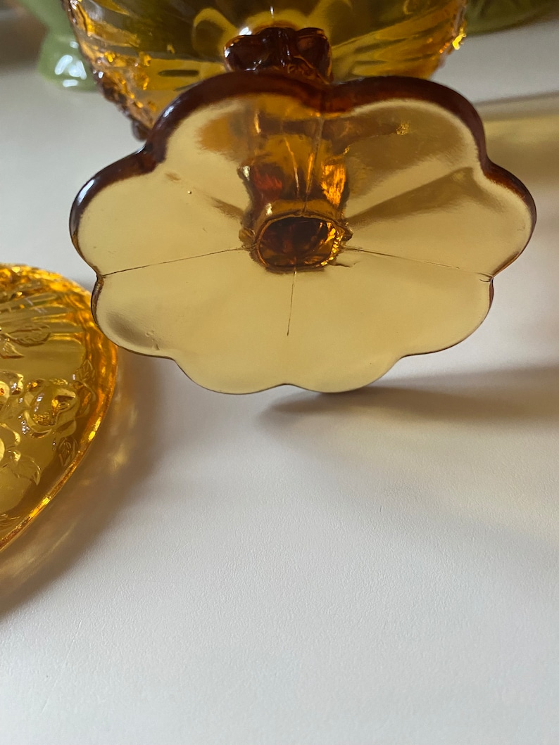 K&ouml;nnte beinhalten: Eine antike Bonbonniere aus bernsteinfarbenem Glas mit floralem Muster. Die Schale hat einen gewellten Rand und einen bl&uuml;tenf&ouml;rmigen Boden.