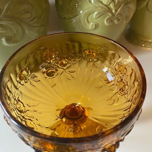 K&ouml;nnte beinhalten: Eine klare, bernsteinfarbene Glassch&uuml;ssel mit geriffeltem Design und Blumenmuster. Die Sch&uuml;ssel hat einen Sockel mit einem gewellten Rand.