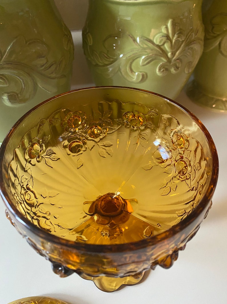 K&ouml;nnte beinhalten: Eine klare, bernsteinfarbene Glassch&uuml;ssel mit geriffeltem Design und Blumenmuster. Die Sch&uuml;ssel hat einen Sockel mit einem gewellten Rand.