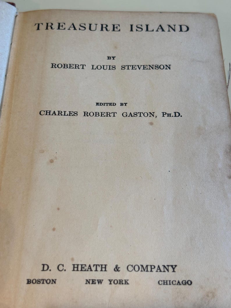 May include: The title page of the book "Treasure Island" by Robert Louis Stevenson. The text is in black font on a cream-colored page. The publisher's name, D.C. Heath & Company, and the cities Boston, New York, and Chicago are also visible.