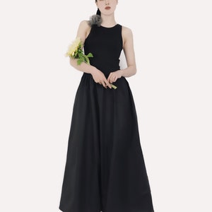 May include: A woman wearing a black sleeveless top and a black maxi skirt. She is holding a bouquet of yellow flowers and wearing green shoes.