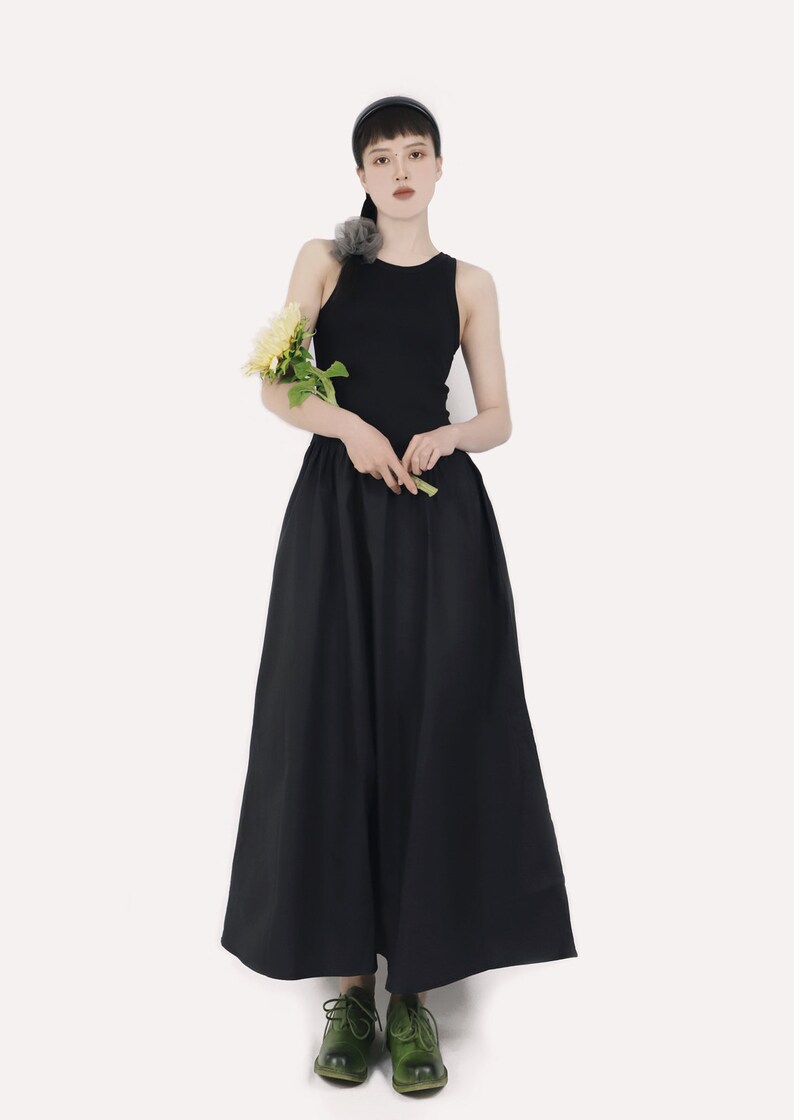 May include: A woman wearing a black sleeveless top and a black maxi skirt. She is holding a bouquet of yellow flowers and wearing green shoes.