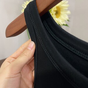 May include: Close-up of the neckline of a black sleeveless top. The top has a double-stitched neckline.