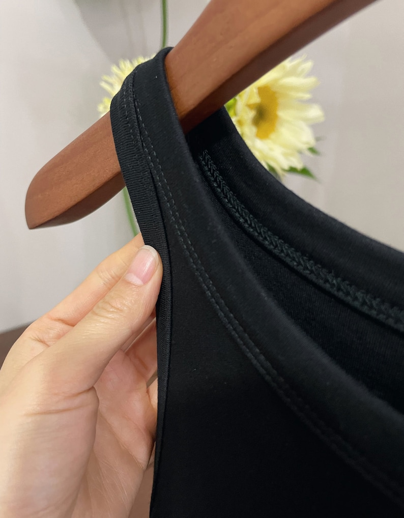 May include: Close-up of the neckline of a black sleeveless top. The top has a double-stitched neckline.