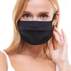 May include: A black face mask made of cotton fabric. The mask has pleats and is worn by a person with blonde hair.