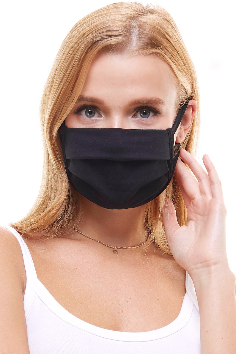 May include: A black face mask made of cotton fabric. The mask has pleats and is worn by a person with blonde hair.