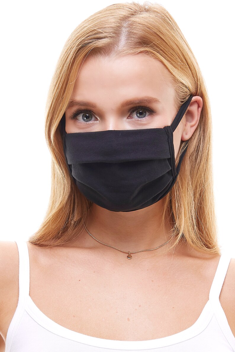 May include: A black face mask with pleats, worn by a person with long blonde hair. The mask has thin straps that go around the ears.