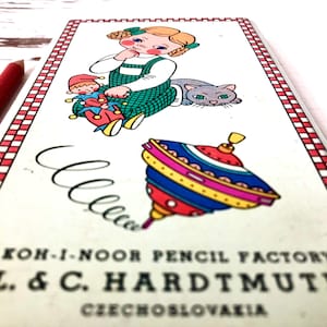 Op de afbeelding: Vintage doos met Koh-I-Noor-potloden van de fabriek L. & C. Hardtmuth in Tsjechoslowakije. De doos heeft een kleurrijke illustratie van een meisje, een clown, een kat en een tol.