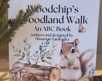 May include: The cover of a children's book titled "Woodchip's Woodland Walk: An ABC Book" written and designed by Shannon Tankesley. The cover features a watercolour illustration of a squirrel holding a green leaf, sitting on a log with mushrooms and flowers.