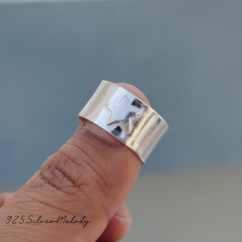 May include: A silver ring with a star design. The ring is worn on a finger.