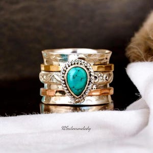 May include: A multi-layered silver ring with gold and copper accents, featuring a teardrop-shaped turquoise stone. The ring has a textured design and the text "925silvermelody" is visible.
