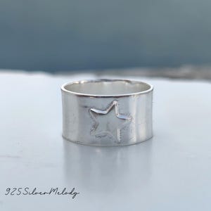 May include: A silver ring with a star design. The ring is wide and has a hammered texture.