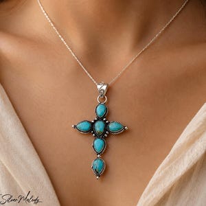 May include: A sterling silver necklace featuring a cross pendant adorned with five teardrop-shaped turquoise stones. The silver setting displays intricate twisted rope detailing around each stone. The pendant hangs from a delicate silver chain.