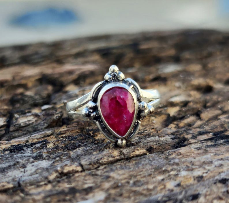 May include: A silver ring with a teardrop-shaped ruby gemstone set in a detailed silver setting.