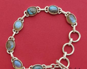 May include: A silver bracelet with oval-shaped labradorite gemstones. The bracelet has a toggle clasp and is made of sterling silver.