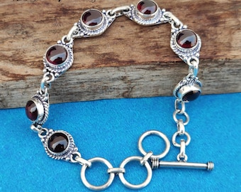May include: A silver bracelet with a toggle clasp features six red gemstone accents. The bracelet is made of 925 sterling silver.