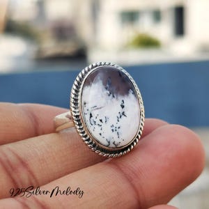 May include: A silver ring with a white and black agate stone set in a rope-like design. The stone has a unique pattern of white and black swirls.