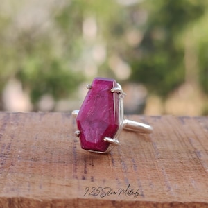 May include: A silver ring with a large, faceted, dark pink gemstone set in a coffin-shaped setting.