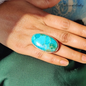 May include: A large oval turquoise ring set in silver. The turquoise is a vibrant blue-green colour with brown and white marbling.