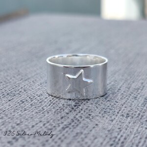 May include: A silver ring with a star design. The ring is wide and has a smooth, polished finish.