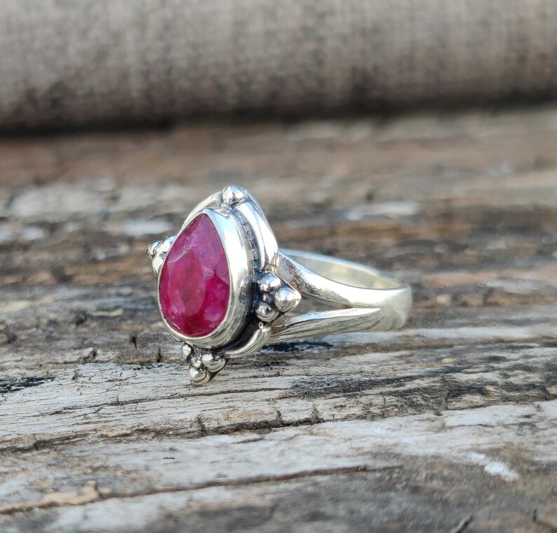 May include: A silver ring with a teardrop-shaped ruby gemstone set in a detailed silver setting. The ring has a delicate, ornate design.