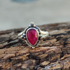 May include: A silver ring with a pear-shaped ruby gemstone. The ring has a delicate design with small beads around the stone.