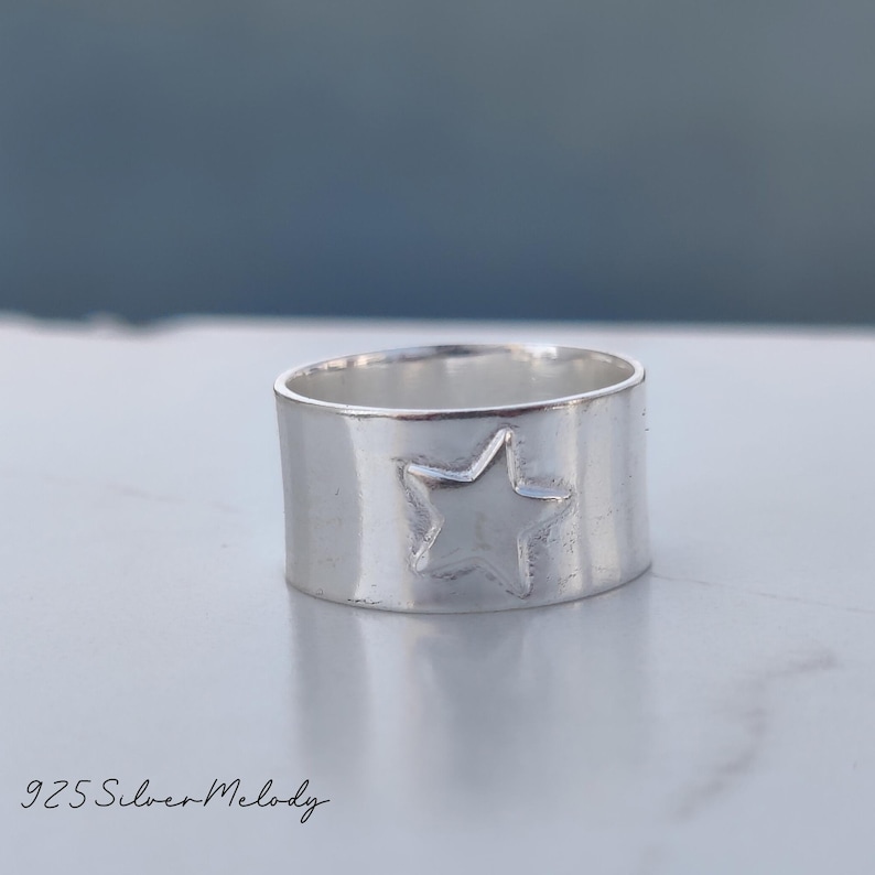 May include: A silver ring with a star design. The ring is wide and has a smooth, polished finish.