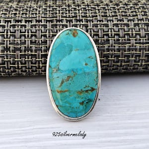 May include: Oval turquoise gemstone ring set in sterling silver. The turquoise is a vibrant blue-green colour with brown marbling.