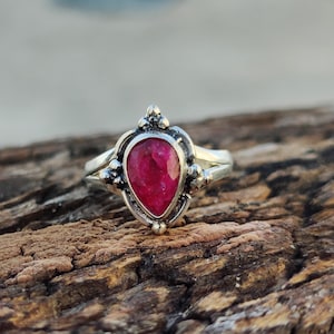 May include: A silver ring with a pear-shaped ruby gemstone. The ring has a delicate design with small beads around the stone.