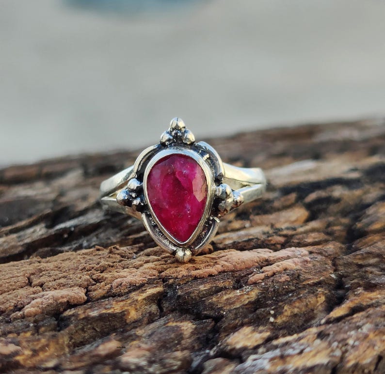 May include: A silver ring with a pear-shaped ruby gemstone. The ring has a delicate design with small beads around the stone.
