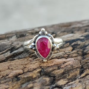 May include: A silver ring with a teardrop-shaped ruby gemstone set in a delicate, ornate design.