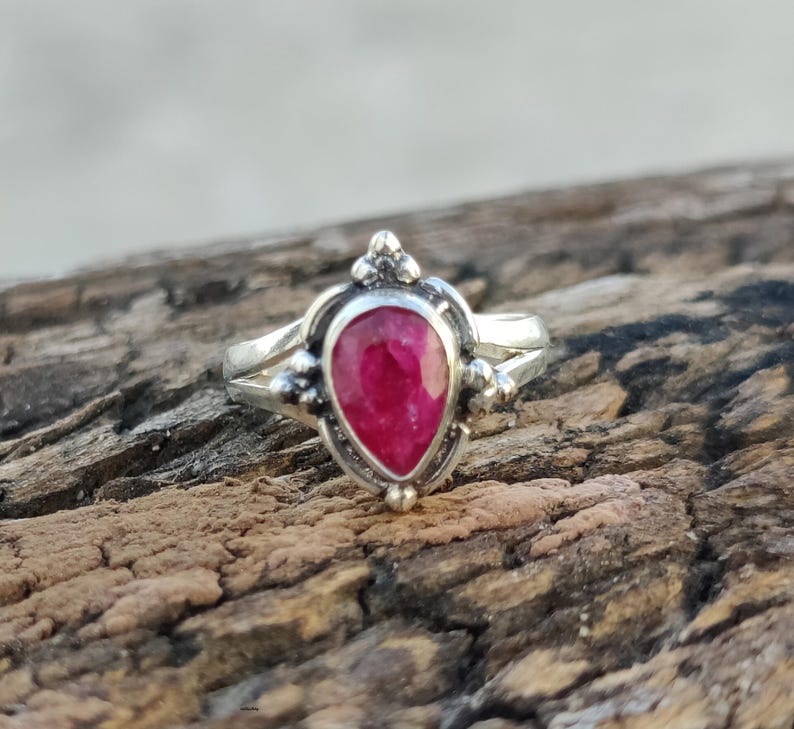 May include: A silver ring with a teardrop-shaped ruby gemstone set in a delicate, ornate design.