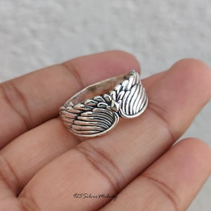 May include: A silver ring featuring a detailed wing design that wraps around the band. The metal has an oxidized finish to highlight the texture of the feathers. The text 925 Silver Melody is printed in the bottom corner of the image.