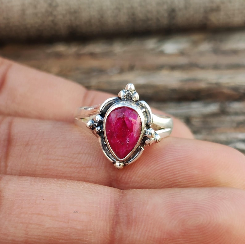 May include: A silver ring with a teardrop-shaped ruby gemstone set in a delicate, ornate design.