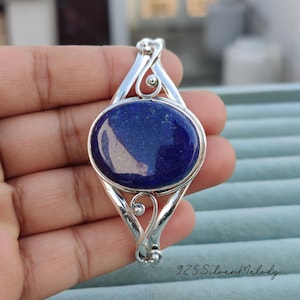 May include: A silver cuff bracelet with a large oval lapis lazuli gemstone. The bracelet has a delicate, ornate design.